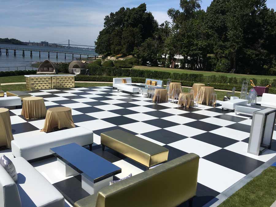 Portable black and white checkered dance floor installed for an outside party with gold and silver furniture