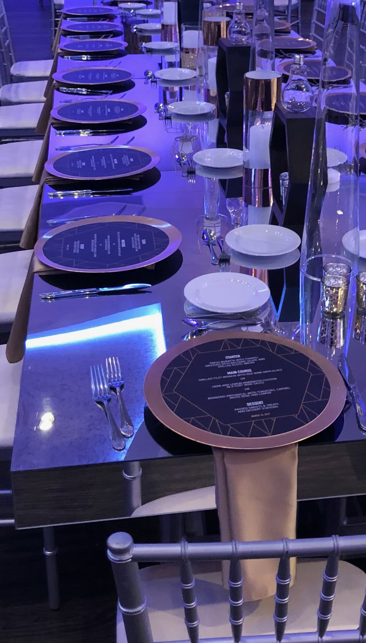 A sweet sixteen dinner table in New York & Long Island shines with purple lighting, candles, and gold accents.