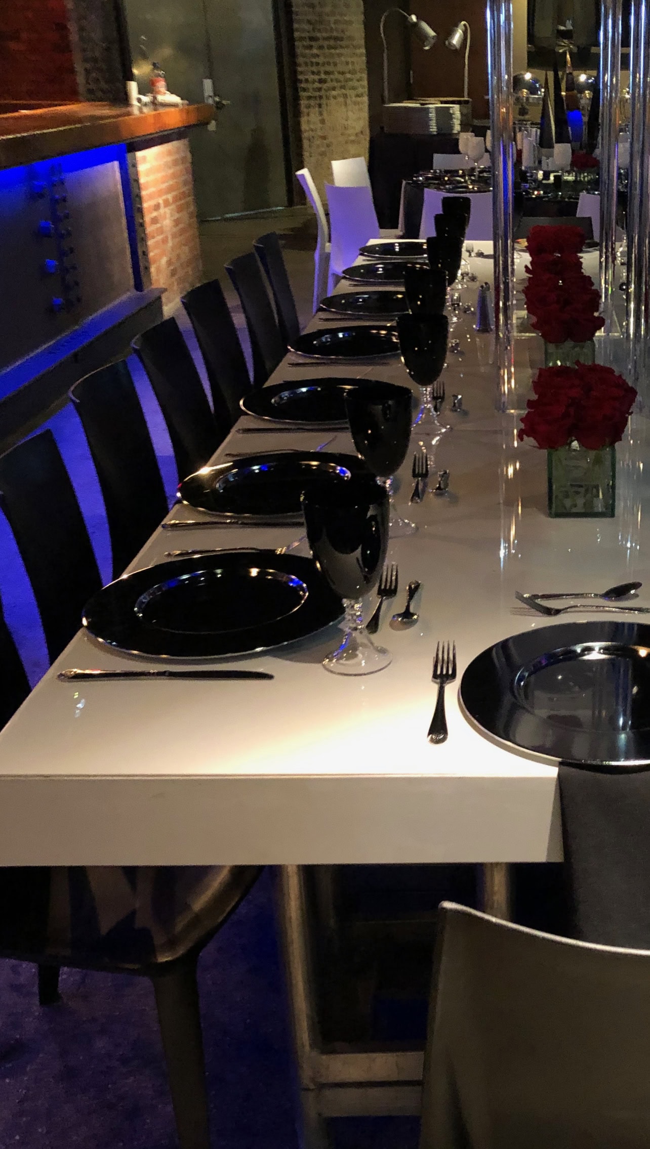 A modern, elegant dining table set for corporate events in New York & Long Island with black plates and red flowers.